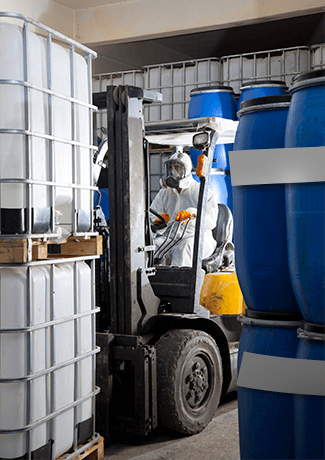 Worker in PPE driving a forklift loaded with chemical storage containers