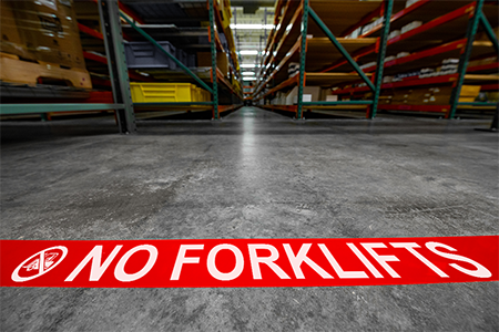A warehouse floor marked with No Forklifts floor marking tape.