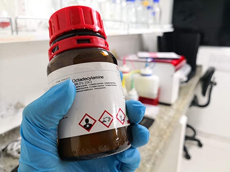 A hand in a rubber glove holding a bottle of octadecylamine  with a correct hazcom label affixed.