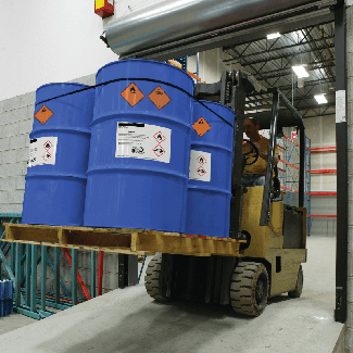 Forklift moving GHS labeled chemical barrels down a ramp