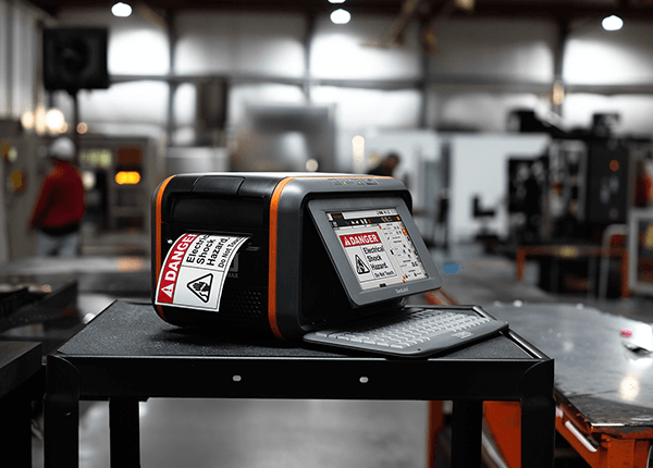 DuraLabel Toro Max printer producing custom safety labels in a mechanical workspace. 