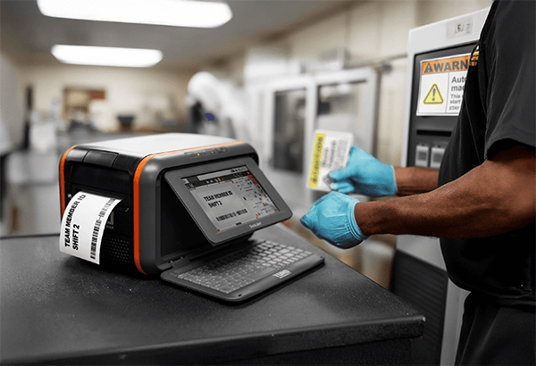 Worker wearing gloves operating a DuraLabel Toro Max printer, printing a shift label in an industrial facility.