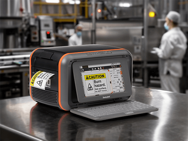 A DuraLabel Toro Max printing a “CAUTION: Burn hazard” label in a clean, stainless steel food manufacturing environment. 
