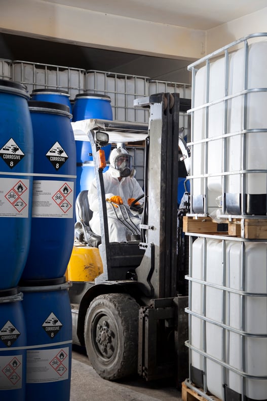 A forklift driver maneuvering chemical barrels and containers clearly marked with safety labels