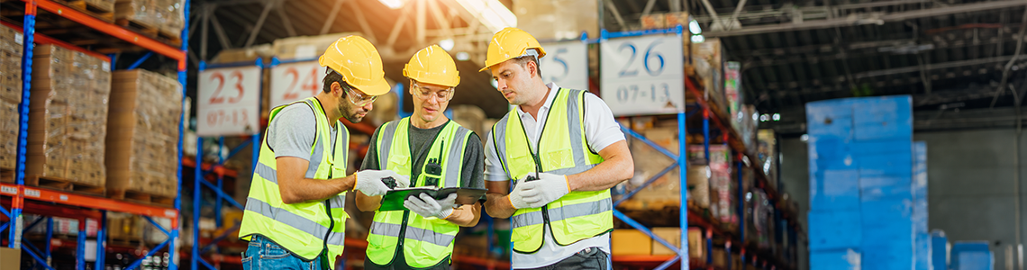 Warehouse workers convene around an open binder to discuss safety.