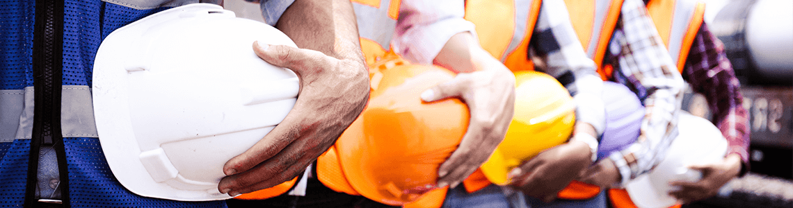 A cropped photo of workers standing in a row holding their hard hats