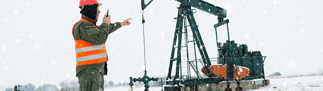 A worker in a snowy oil field speaking into a radio while pointing at equipment