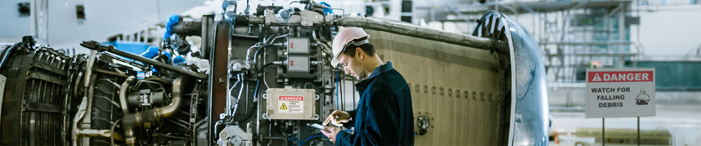 A worker runs diagnostics on an aircraft with a safety label prominently displayed on the craft and a safety sign in the hanger.