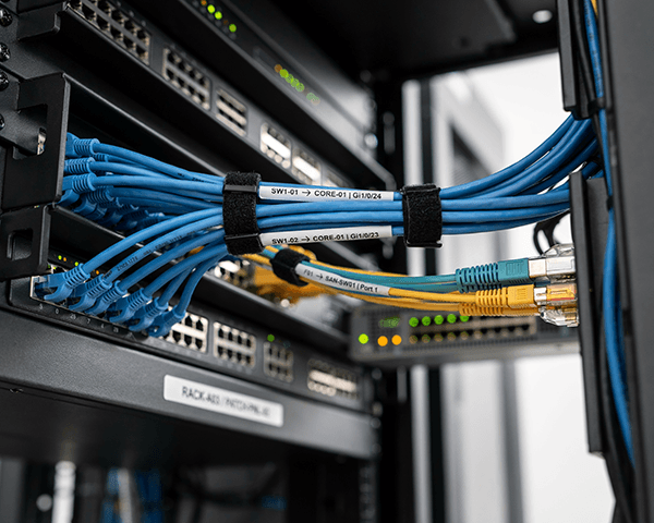 Close-up of cable labeling on blue network cables connected to switches inside a server rack.