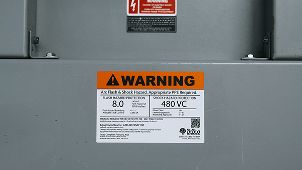 Close-up of an arc flash electrical safety label showing voltage and PPE requirements on industrial equipment.