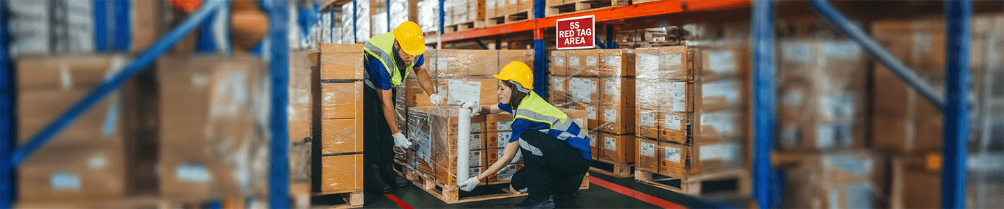 Workers in hard hats move pallets in a warehouse 5S red tag area with stacked boxes