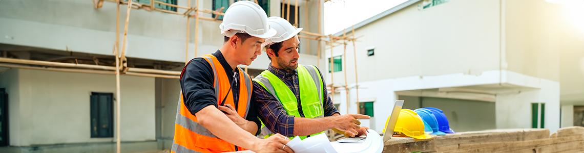 Two construction workers looking at a laptop on a job site.