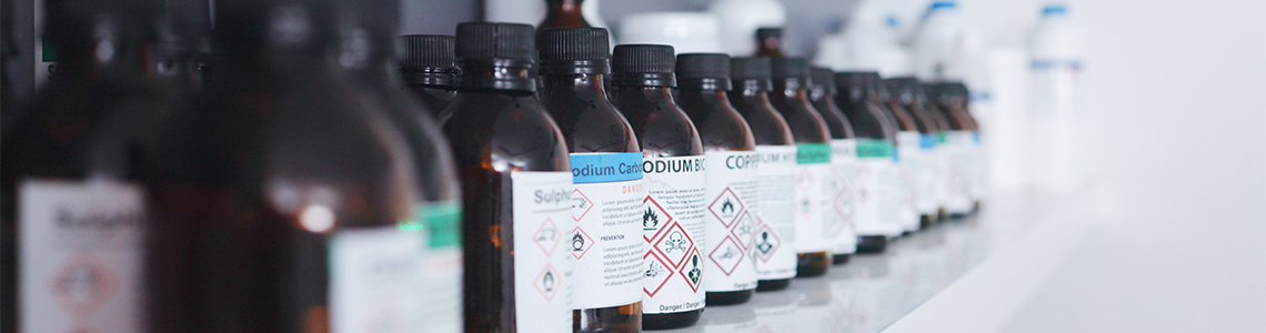 A row of brown glass bottles with GHS labels on them in a Lab setting.