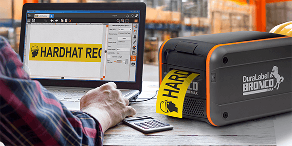 DuraLabel Bronco Max industrial label printer producing a yellow “Hardhat Required” label beside a laptop.