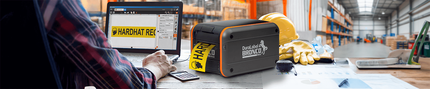 DuraLabel Bronco Max industrial label printer producing a yellow “Hardhat Required” label beside a laptop.