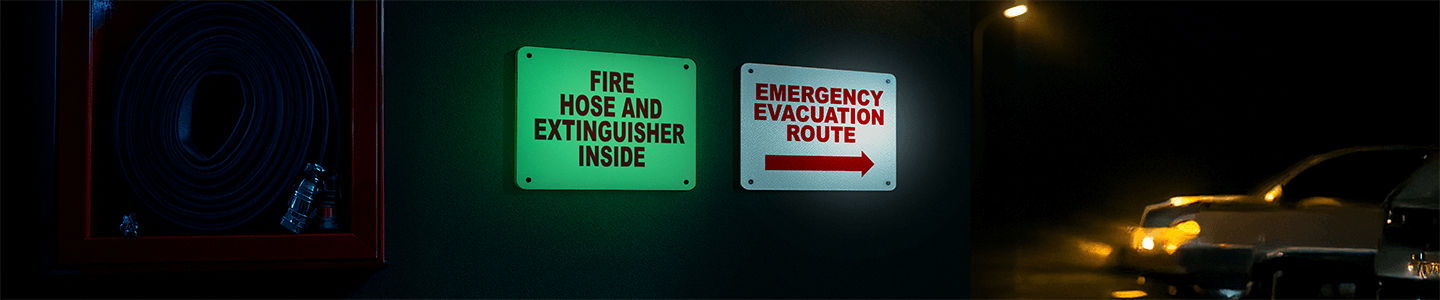 Glow-in-the-dark and reflective emergency fire signs mounted in a low-light corridor, showing clear evacuation route labeling.