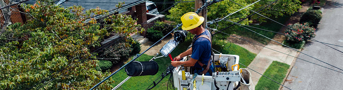A worker is performing a repair on electrical lines while standing in a cherry picker bucket