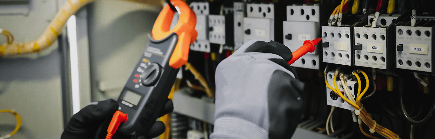 Gloved hands using tools to measure electrical equipment