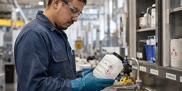 Worker inspecting secondary container labels on a chemical bottle in an industrial facility.