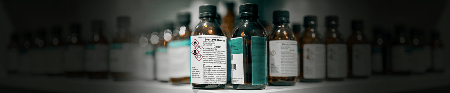Worker inspecting secondary container labels on a chemical bottle in an industrial facility.
