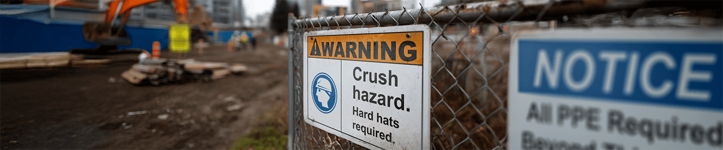 Warning sign on a fence reading “Crush hazard. Hard hats required” at a construction site.