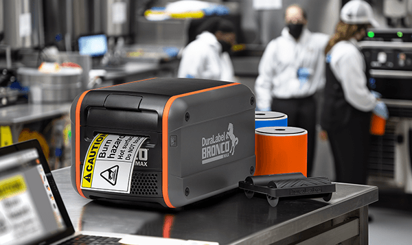 Bronco Max safety label printer with supplies, printing a caution label in a clean industrial setting.