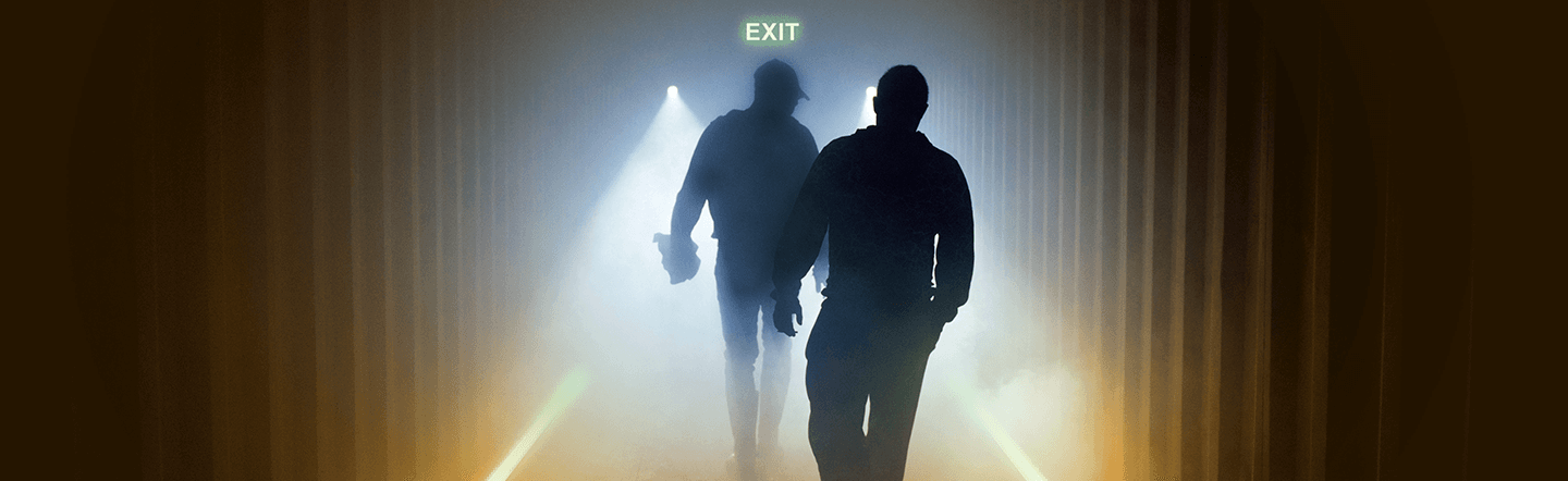 Two workers walking down a dark, smoky hallway, following glowing floor marking.