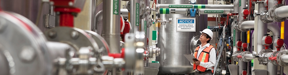 A safety inspector examines piping and storage tanks in an industrial facility