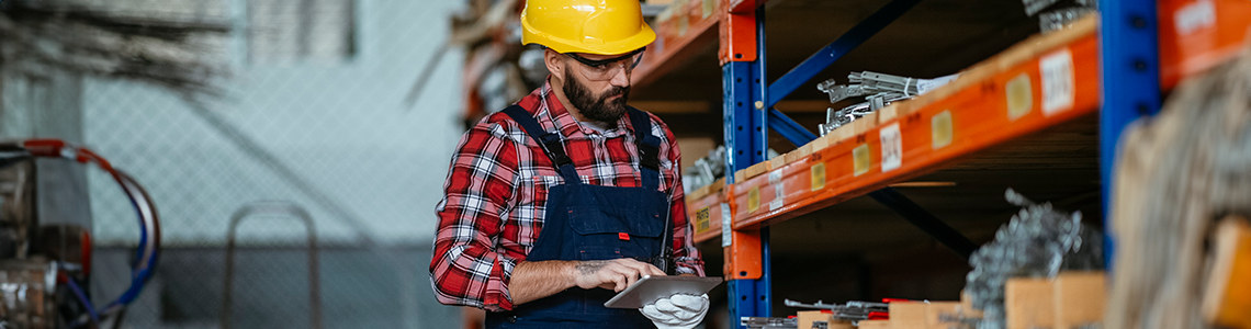 A man using a tablet to inventory and organize in a warehouse.