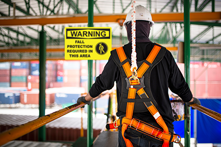 Worker walking on a suspended platform holding the railing. They are wearing a safety harness.