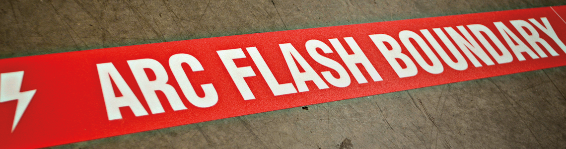 A large, printed label sign affixed to concrete warns of an arc flash boundary.