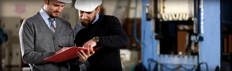 Workers discuss a document while standing on the floor of a warehouse.