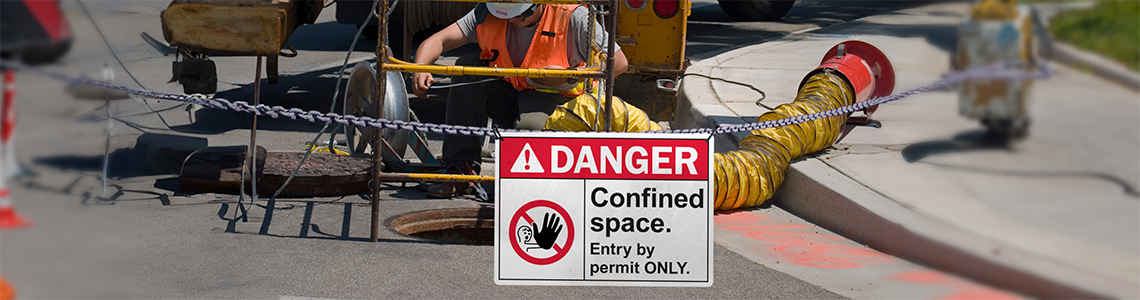 A danger confined spaces is the foreground with a worker descending into a small tunnel pictured in the background.