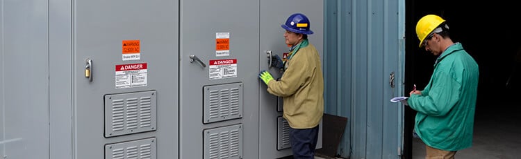 A worker is accessing and electrical panel clearly marked with safety signs and labels.