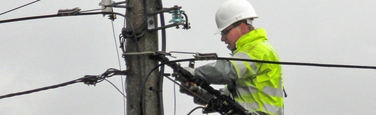 A lineman works on powerlines while wearing PPE