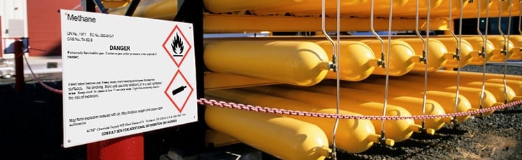 Steel methane gas cylinders are stacked and marked with warning sign labels.