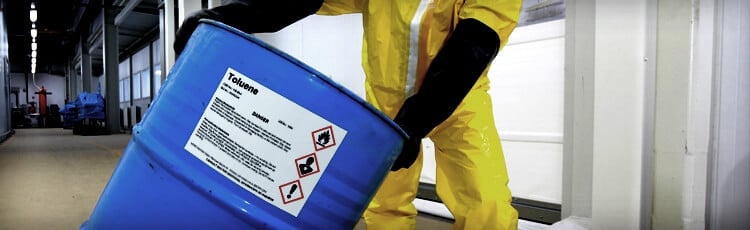 A worker in PPE moves a chemical barrel with a OSHA compliant label