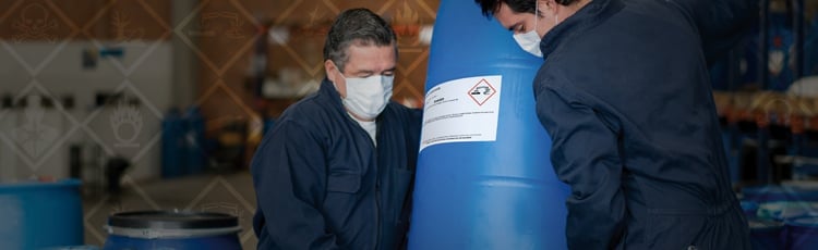 Workers Moving a Chemical Barrel with GHS labeling