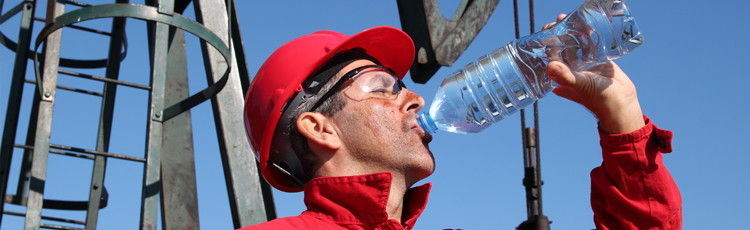 A worker in a hardhat drinking water to stay hydrated and mitigate effects of heat exposure