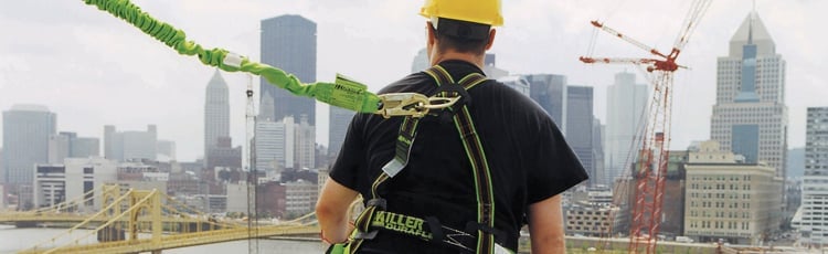 A construction worker is wearing PPE and a safety harness while building a sky scraper