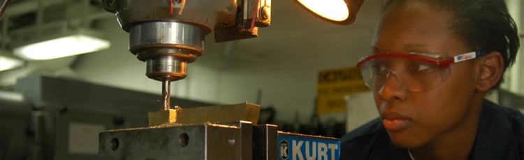 A woman operates a drill press in a machine shop.