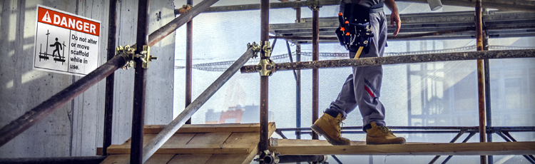 A worker walks on scaffolding wearing PPE and observing a large Danger Scaffolding sign.